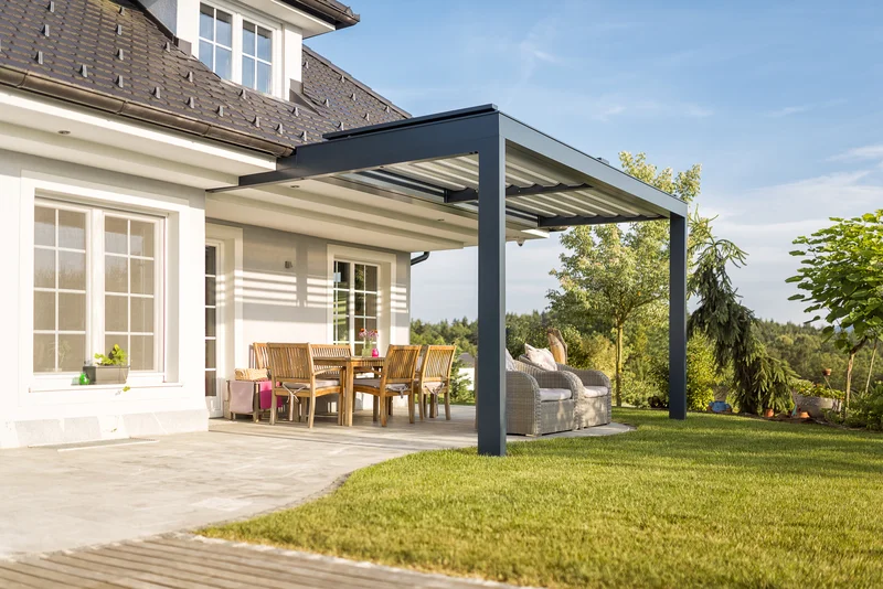 Paved concrete patio under a modern black pergola next to lawn. Paved concrete patio under a modern black pergola next to lawn.