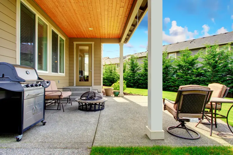 Covered backyard patio with smooth concrete slab floor and grill